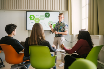 Student am Whiteboard, im Vordergrund drei Studierende, die ihm zuhören